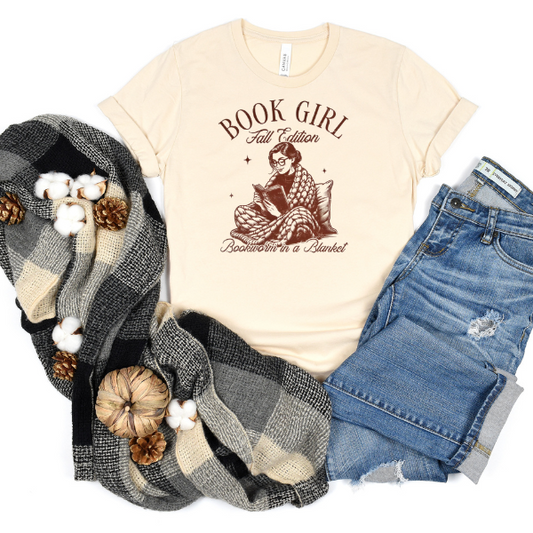 A beige t-shirt with 'Book Girl' text and a graphic, blue jeans, a plaid scarf, and white cotton pearls.