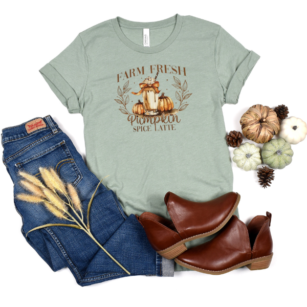 A green t-shirt with 'Farm Fresh Pumpkin Spice Latte' text and a graphic of pumpkins, placed next to blue jeans and brown ankle boots.