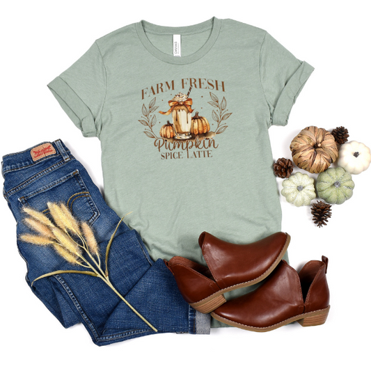 A green t-shirt with 'Farm Fresh Pumpkin Spice Latte' text and a graphic of pumpkins, placed next to blue jeans and brown ankle boots.