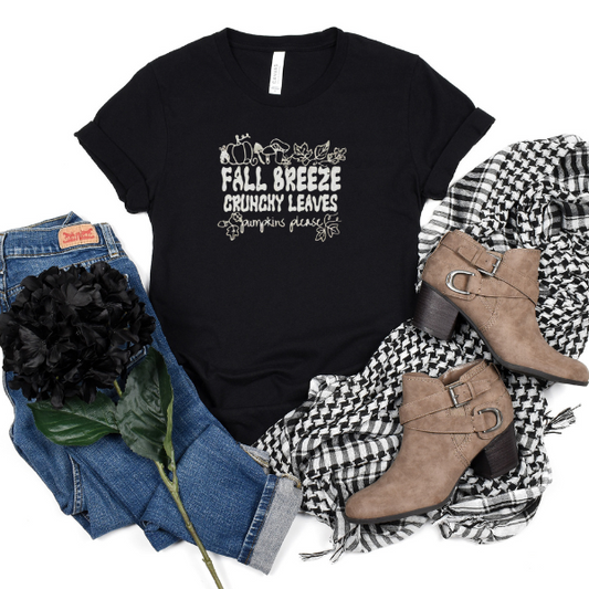 A black t-shirt with text 'Fall Breeze Crunchy Leaves' printed on it, accompanied by a brown checkered scarf, blue denim jeans, and brown ankle boots.