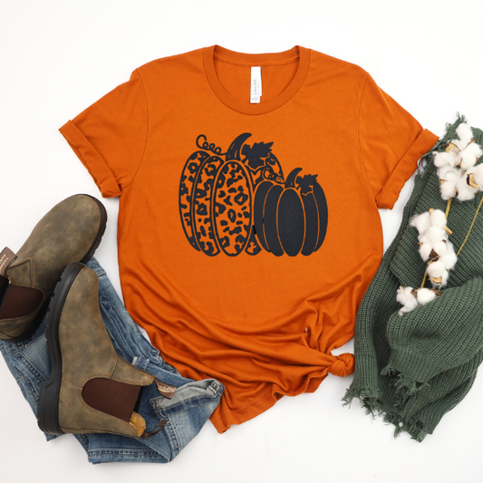 An orange shirt with a pattern of pumpkins and leaves, paired with blue jeans, brown boots, a green scarf, and white cotton towels.